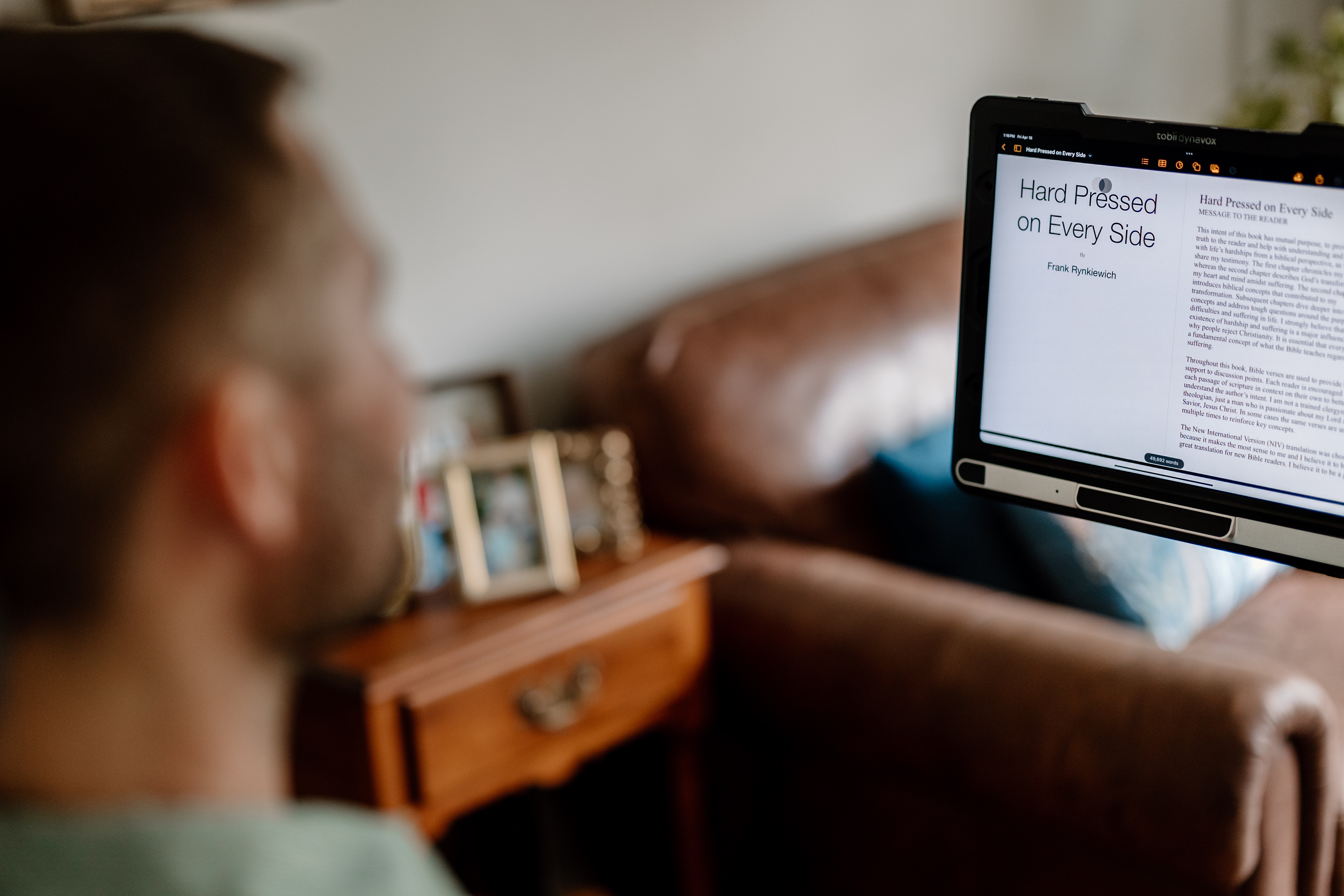 Frank writing 'Hard Pressed on Every Side' by Frank Rynkiewich displayed on a Tobii Dynavox assistive device screen.