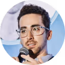 Man with glasses speaking into a microphone.