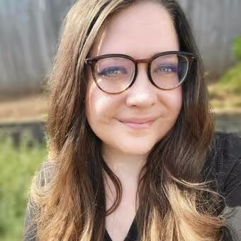 Portrait of a smiling woman with long brown hair and glasses wearing a black top.
