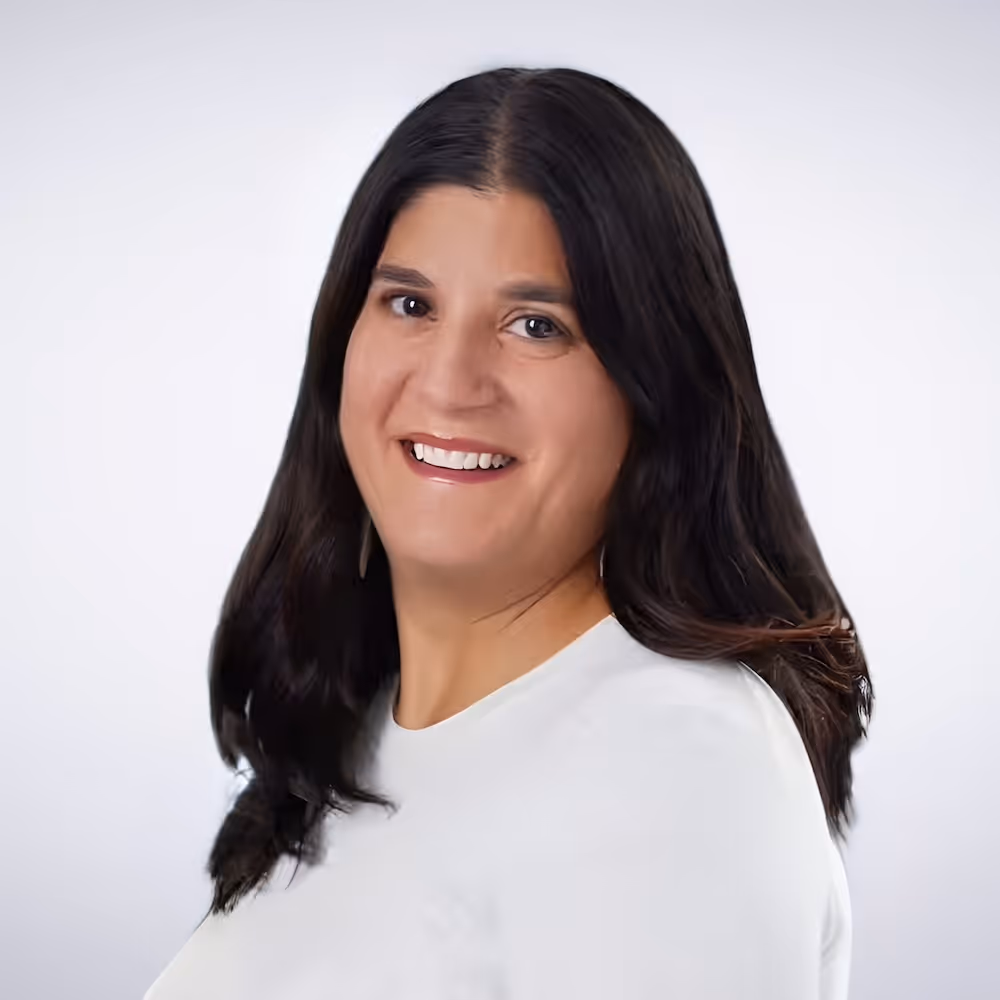 Smiling woman with long dark hair wearing a white top against a light background.
