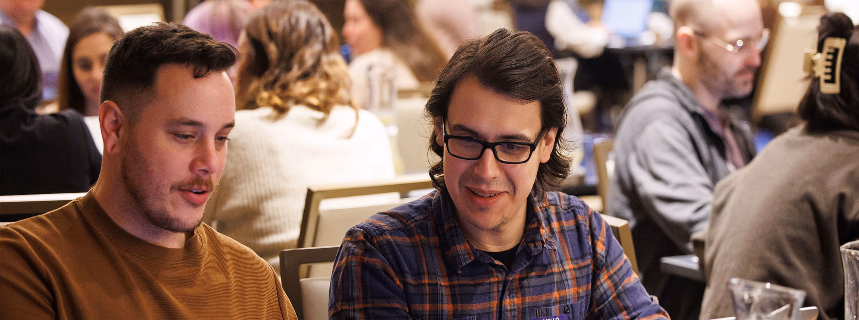 Two men sitting at a table engaged in conversation in a busy indoor setting.