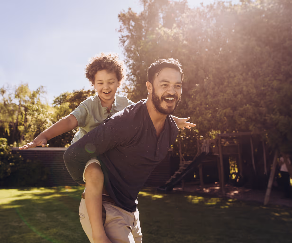 Smiling young woman giving a piggyback ride to a teenage girl outdoors on a sunny day.