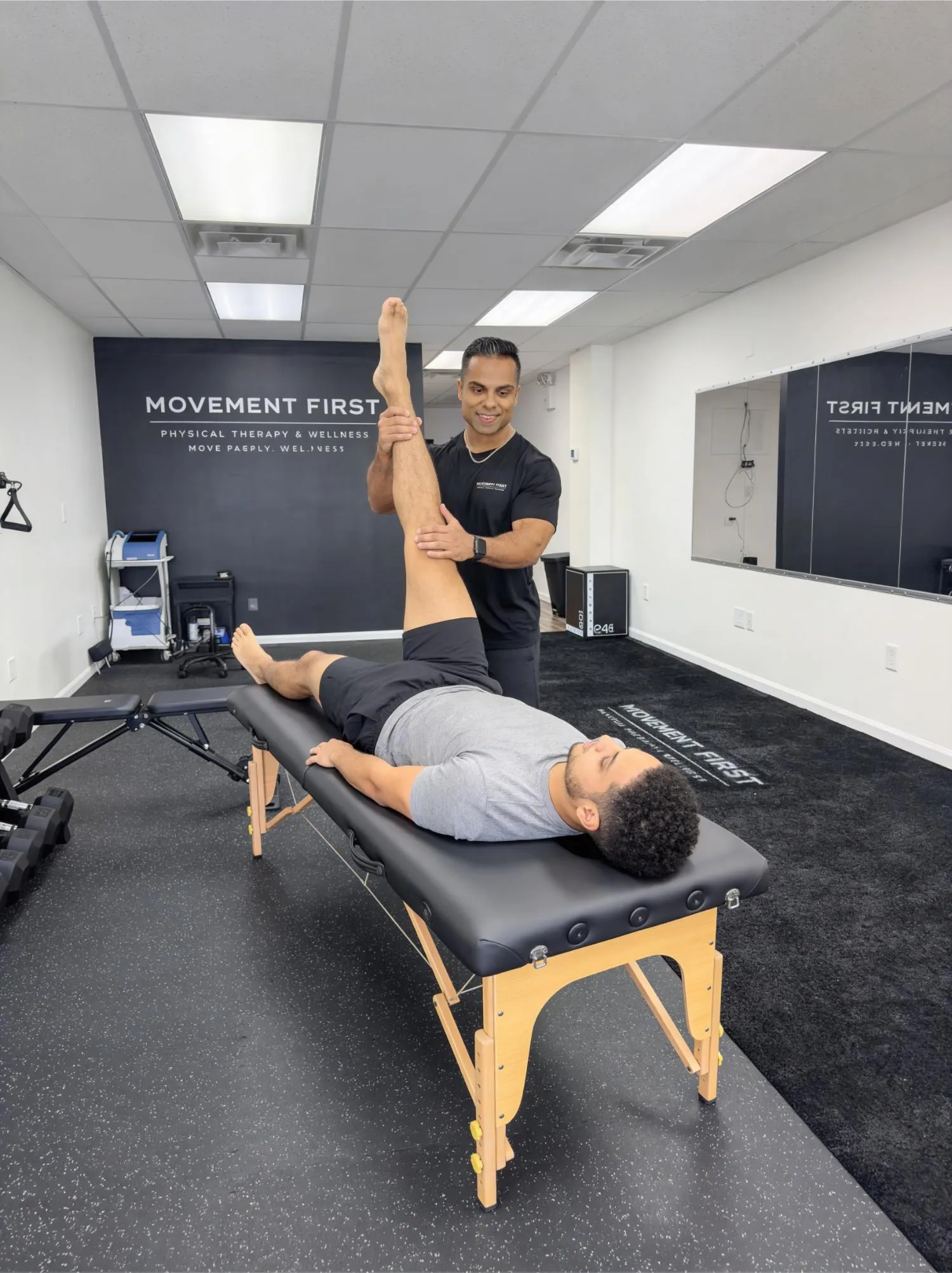 Therapist stretches a man's leg as he lies on a treatment table in a physical therapy clinic.
