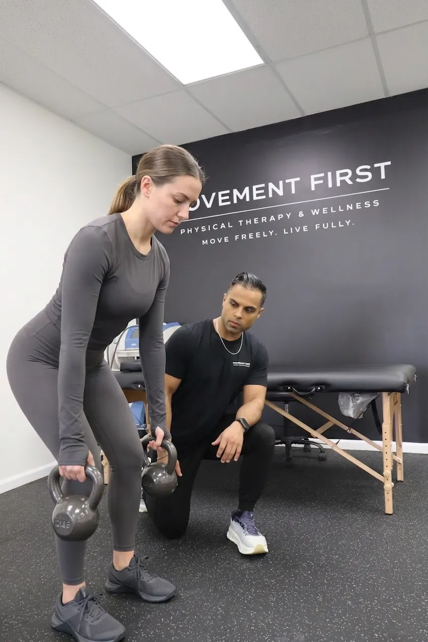 Woman lifting kettlebells under the guidance of a trainer in a physical therapy and wellness clinic.