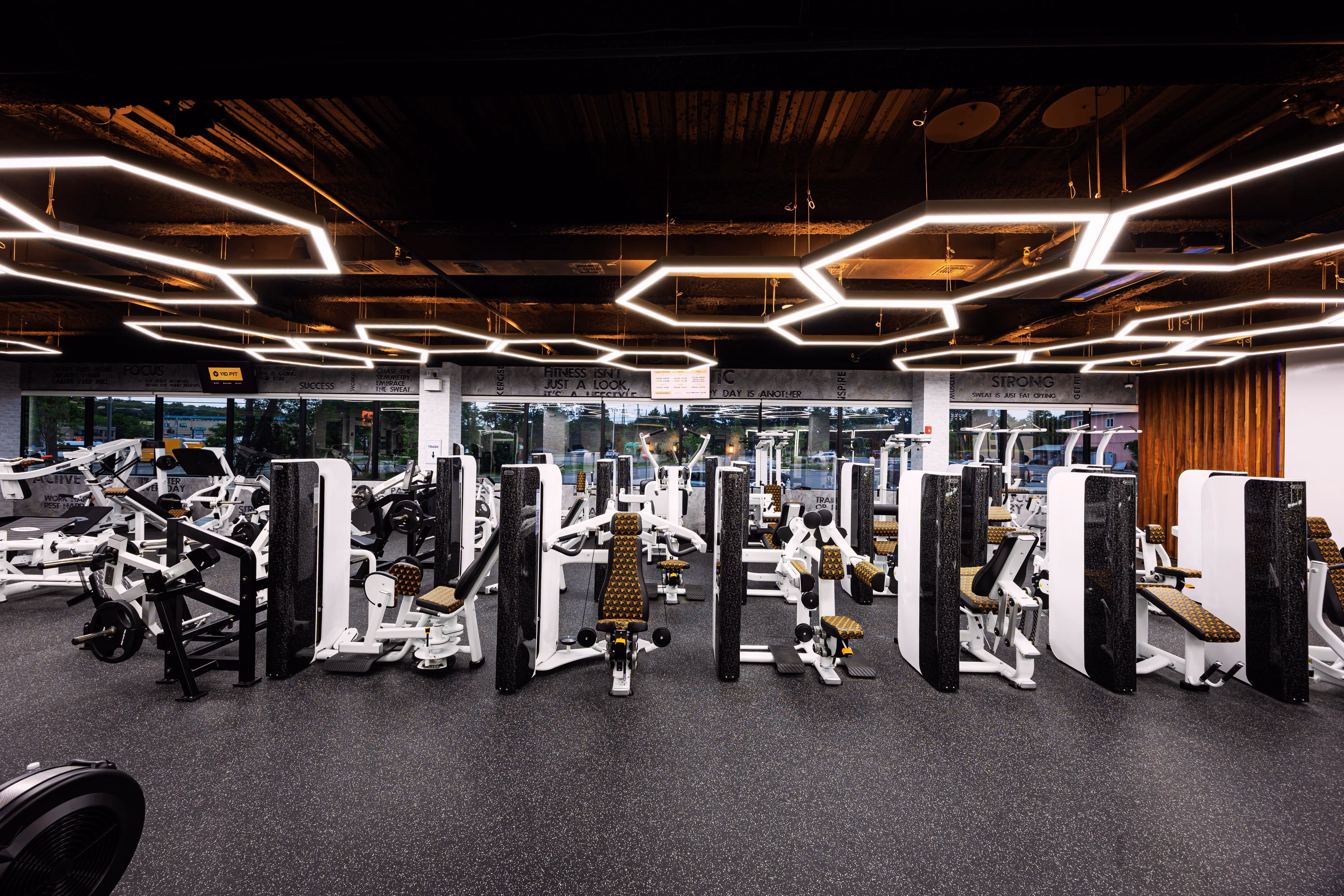 Modern gym interior with weightlifting machines, benches, and geometric ceiling lights.