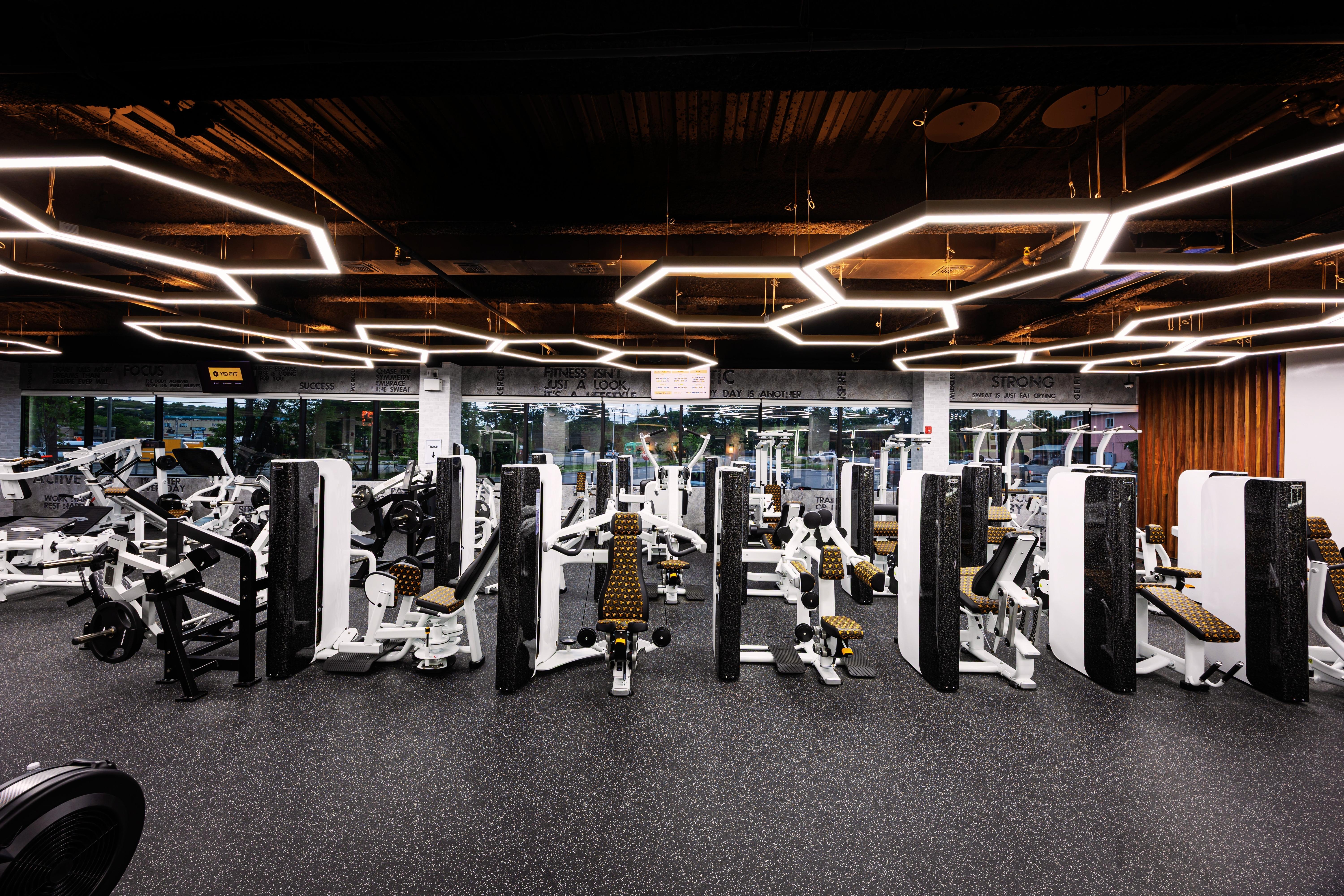 Modern gym interior with weightlifting machines, benches, and geometric ceiling lights.