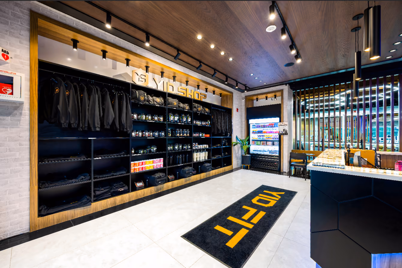 Retail display wall with neatly arranged hoodies, hats, sweatshirts, sneakers, and water bottles under warm lighting.