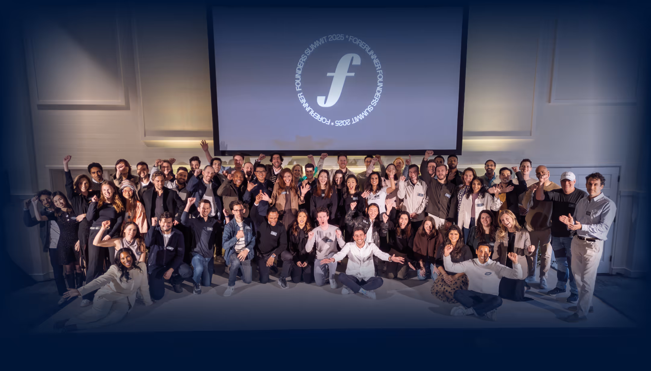 Large group of diverse people smiling and raising their fists together in front of a screen displaying the Forerunner Founders Summit 2025 logo.