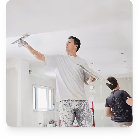 Zwei Handwerker verputzen eine helle Zimmerdecke, einer streicht mit einer Glättkelle, der andere arbeitet mit dem Rücken zur Kamera.