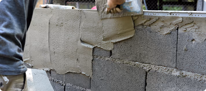 Person glättet frischen Zement auf eine Mauer aus Betonblöcken.
