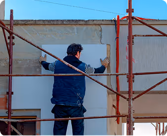 Mann auf einem Baugerüst, der eine weiße Platte an eine Wand hält.
