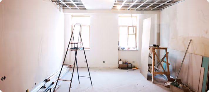 Renovierungsarbeiten in einem Raum mit unvollständiger Decke, Leitern und Baumaterialien auf dem Boden.