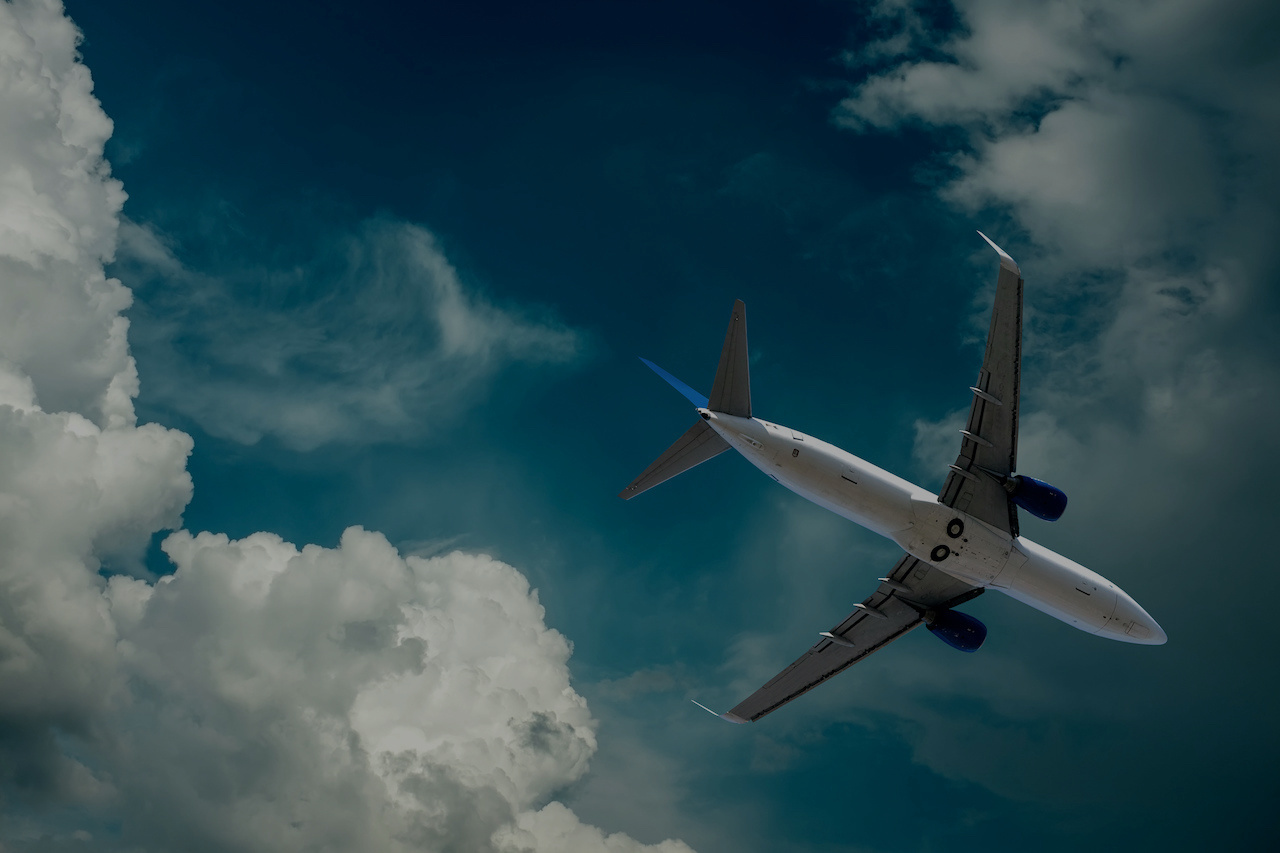 Commercial airplane flying in a blue sky with large white clouds.
