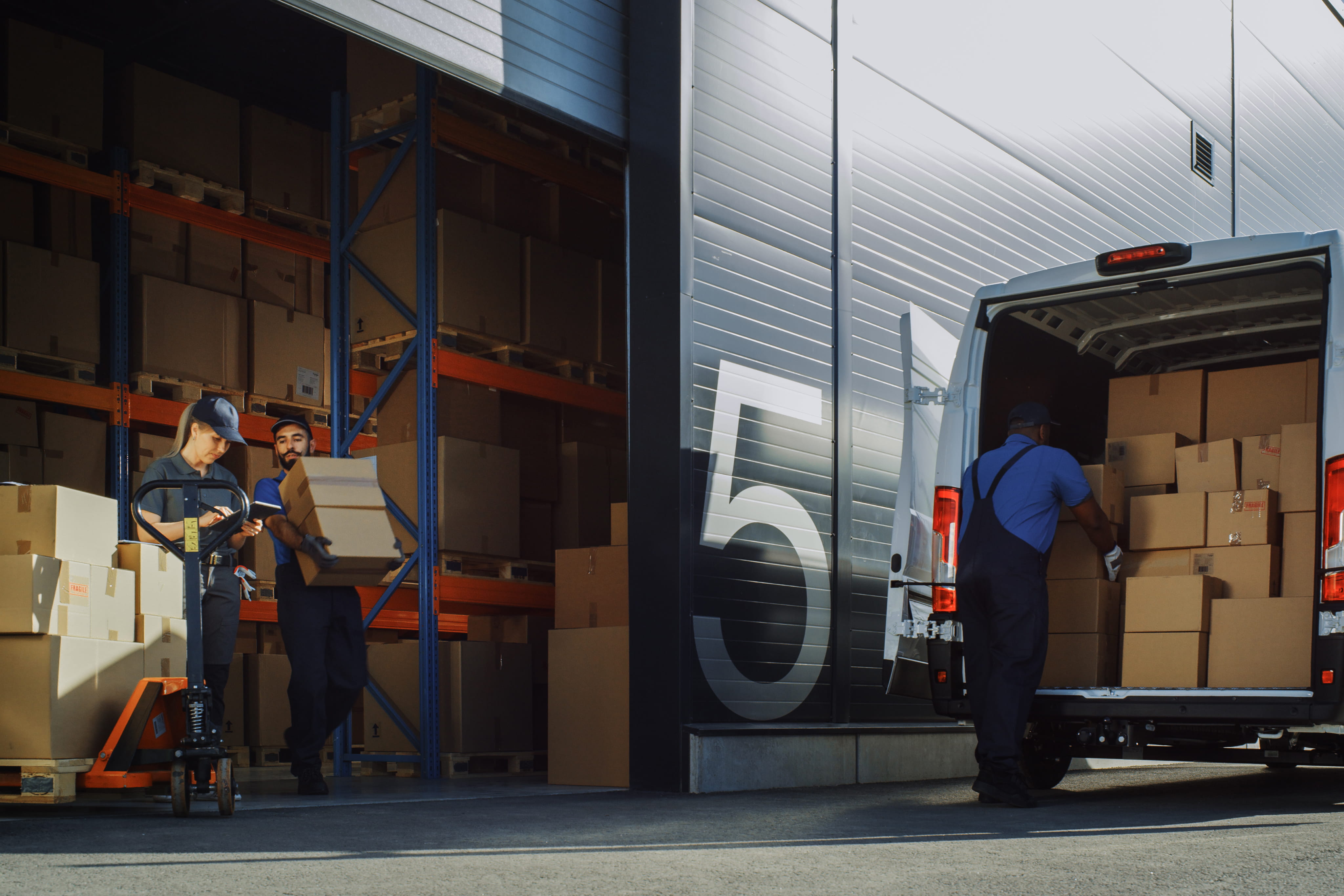 Workers loading and unloading cardboard boxes between warehouse and delivery van.