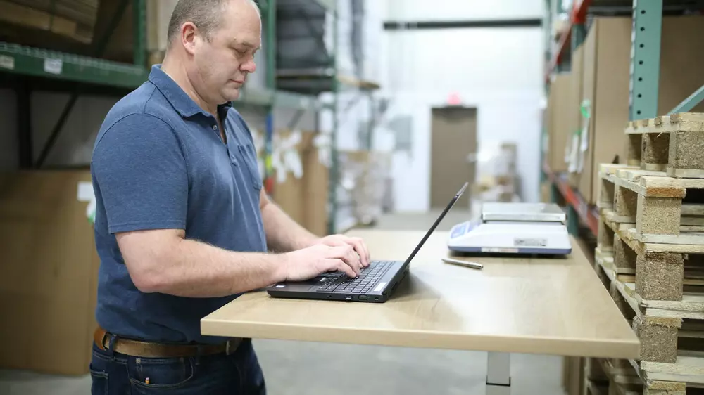 An operations manager working on a laptop at a standing desk in a warehouse
