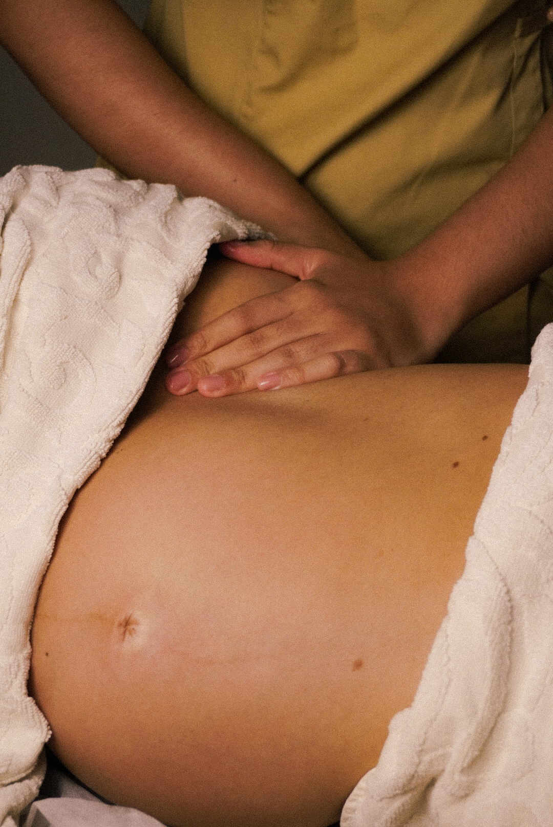 Hands gently massaging the bare belly of a pregnant person covered partially by a white towel.
