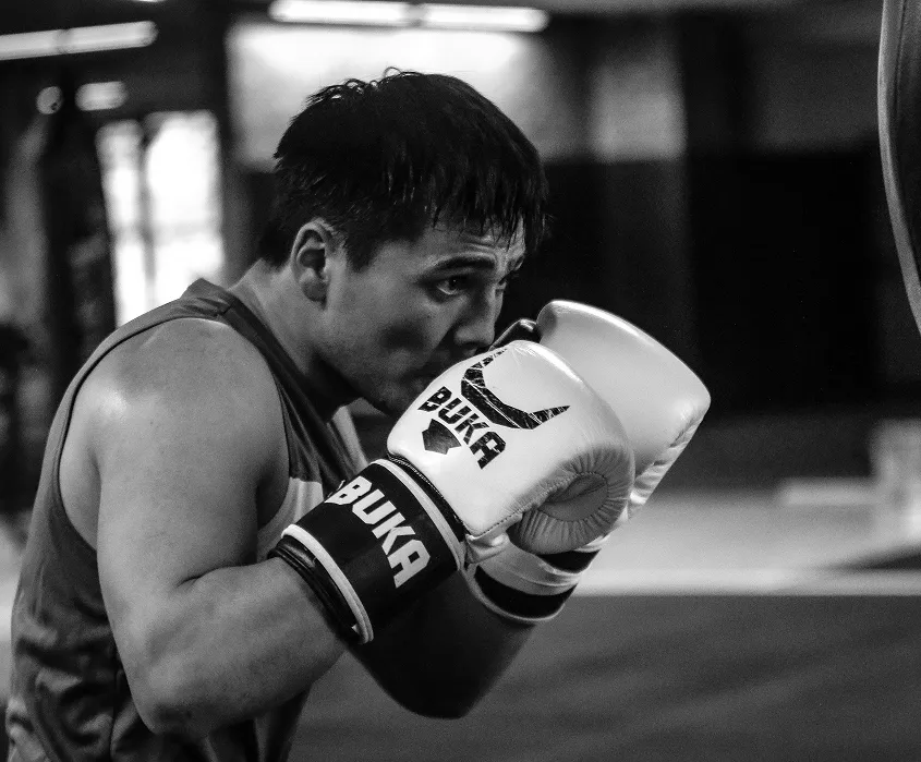 Boxer wearing Buka branded gloves in a fighting stance inside a gym.