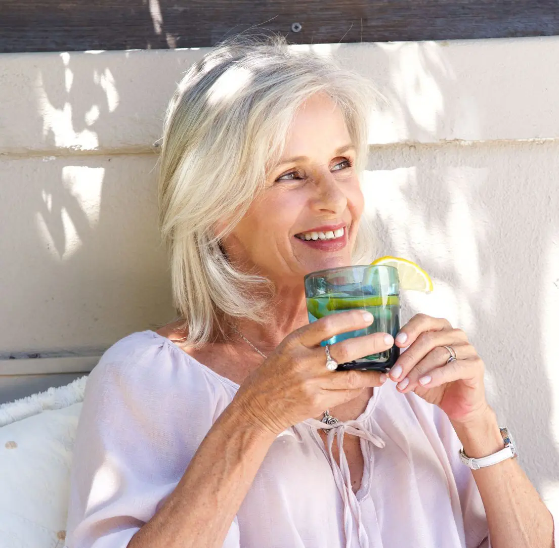 older woman smiling and drinking from a glass