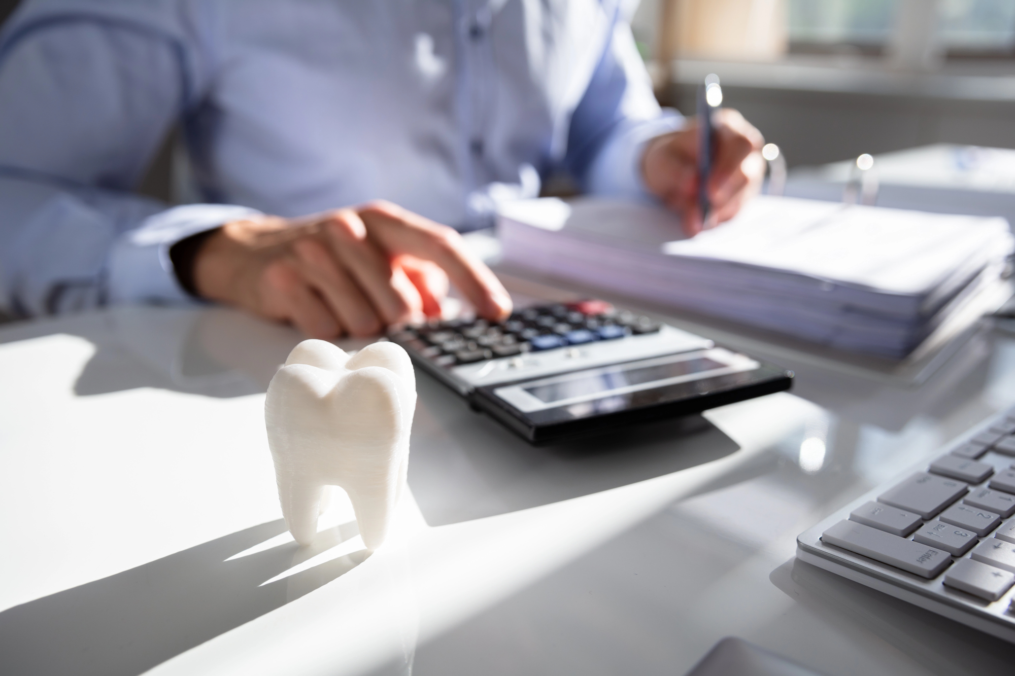 man using calculator next to a model of a tooth