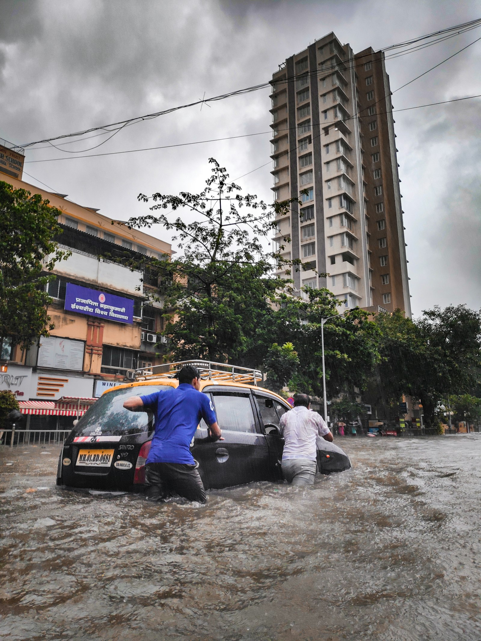 Two people pushing a taxi through floodwater on a city street