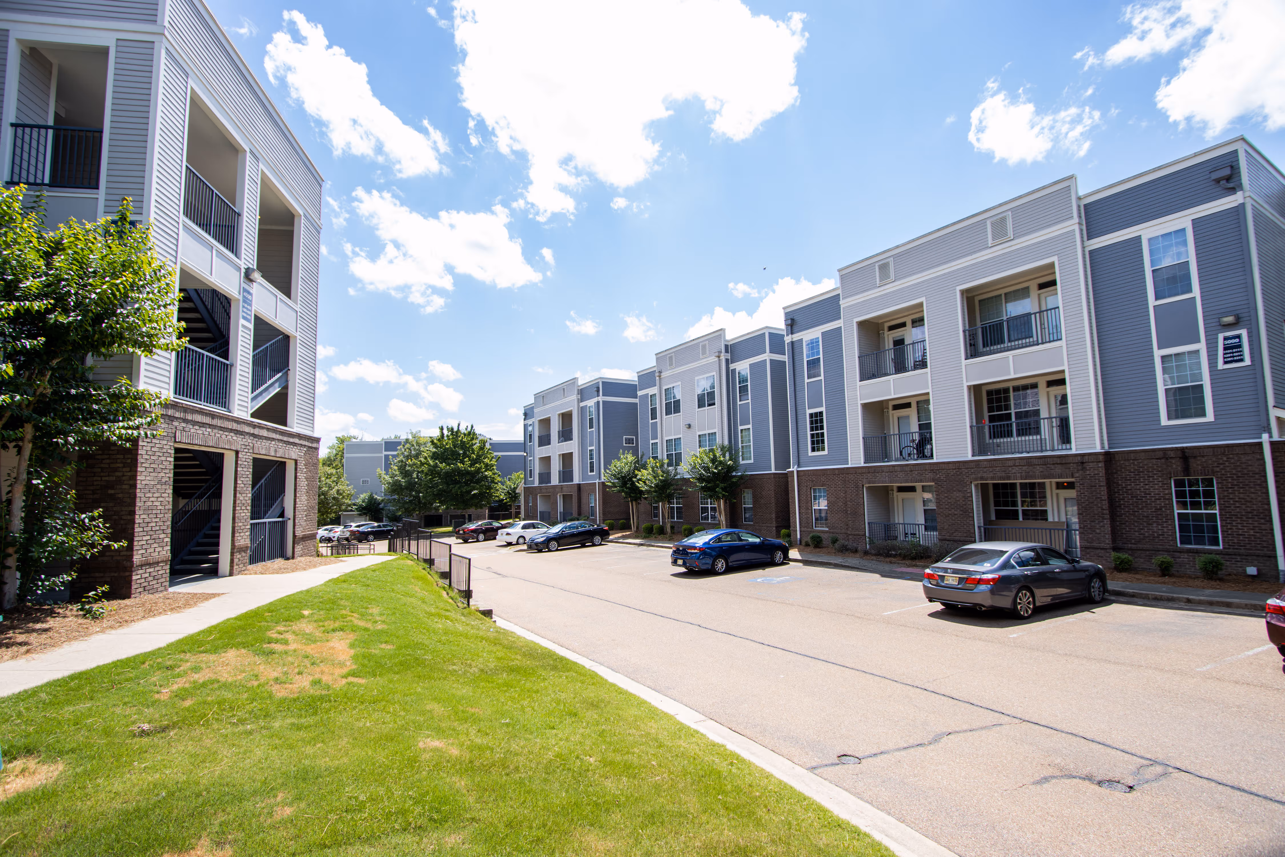 Exterior view of the modern gray and blue apartment buildings and parking lot, showcasing the community layout at Rev Oxford in Oxford, MS.