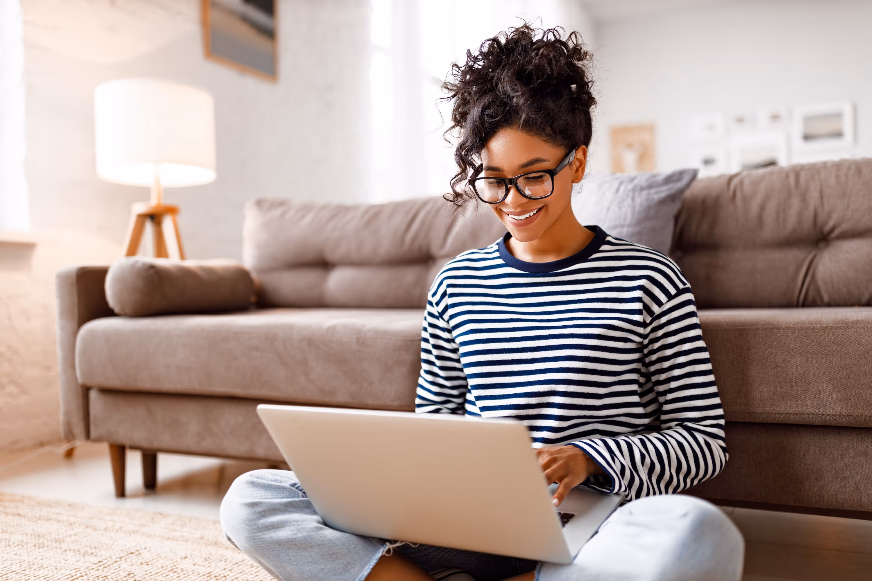 Smiling resident sitting on the floor and working on a laptop in a bright, modern living room at Rev Oxford, highlighting open floor plans and flexible spaces for remote work or study in Oxford, MS.