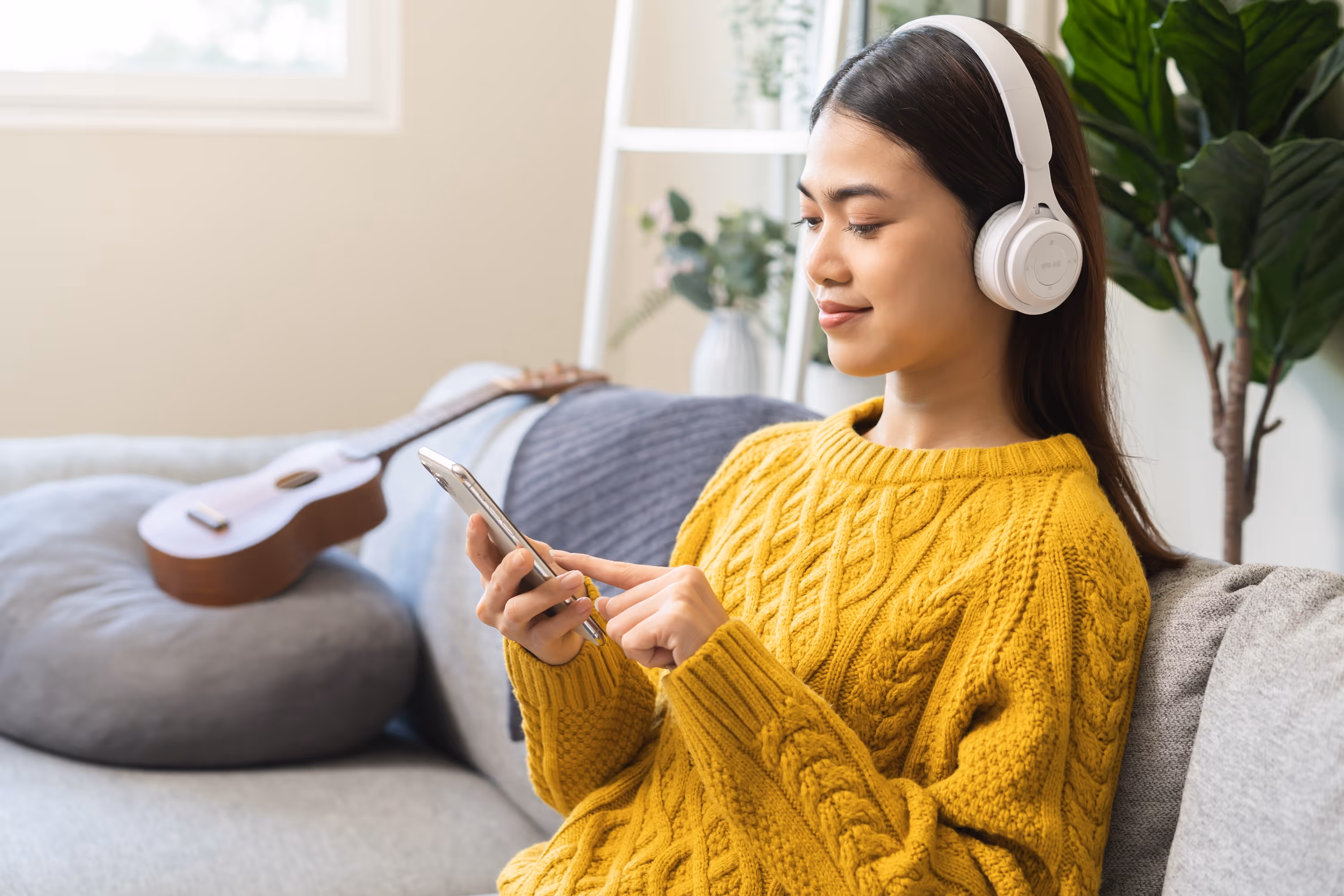 Person wearing headphones and using a smartphone while relaxing in a modern apartment living room at Rev Oxford.