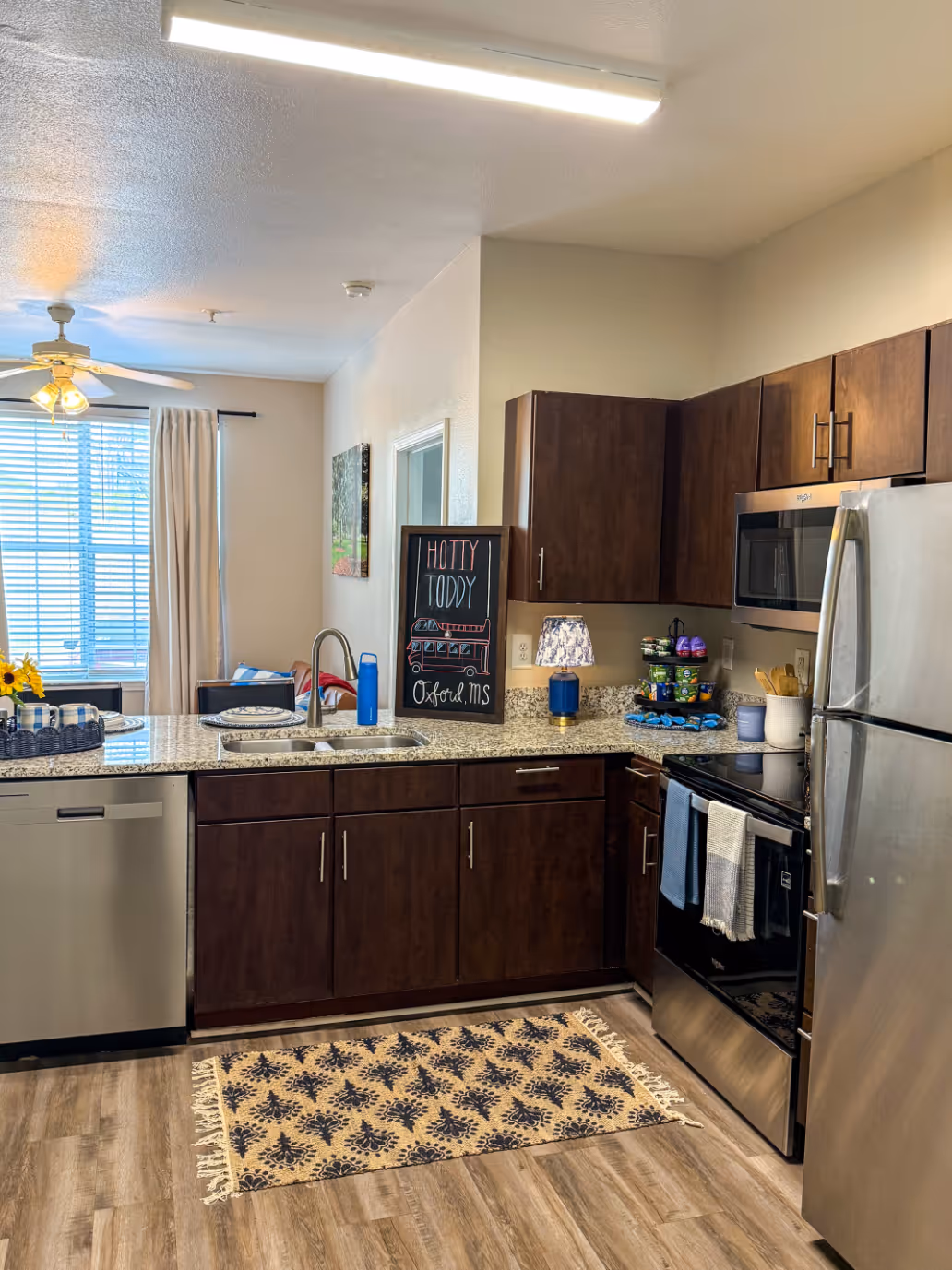 Open-concept apartment living room with a sofa, coffee table, and a view into bedroom with bed and of kitchen bar at Rev Oxford in Oxford, MS.