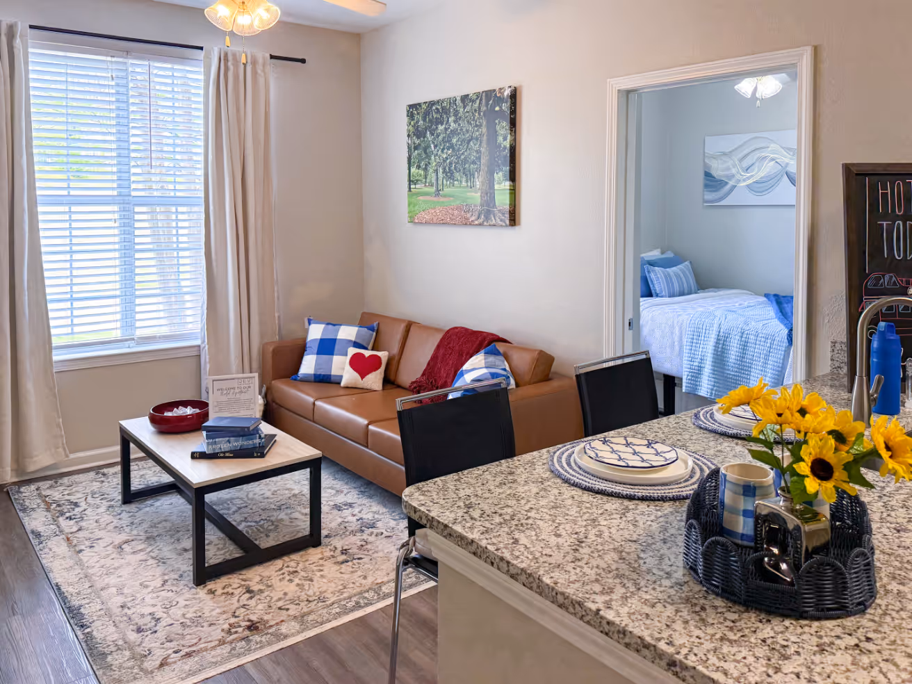 Apartment living room with a brown sofa, floral rug, and contemporary wall art, showcasing a home interior at Rev Oxford in Oxford, MS.