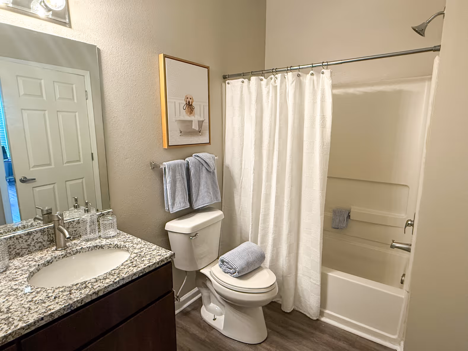 Apartment bathroom with a dark wood vanity, granite countertop, and a shower/tub combo with a blue and white curtain at Rev Oxford in Oxford, MS.
