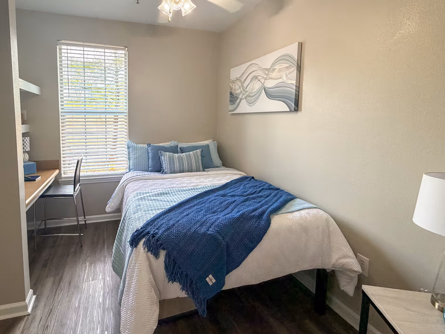 Student apartment bedroom with a bed, desk, featuring a vibrant modern wall art at Rev Oxford in Oxford, MS.