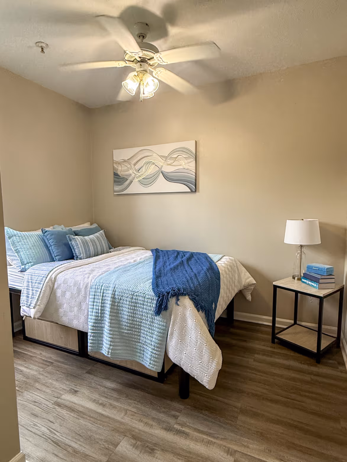 Student apartment bedroom with a bed, desk, and bedside table, featuring a vibrant modern wall art at Rev Oxford in Oxford, MS. 