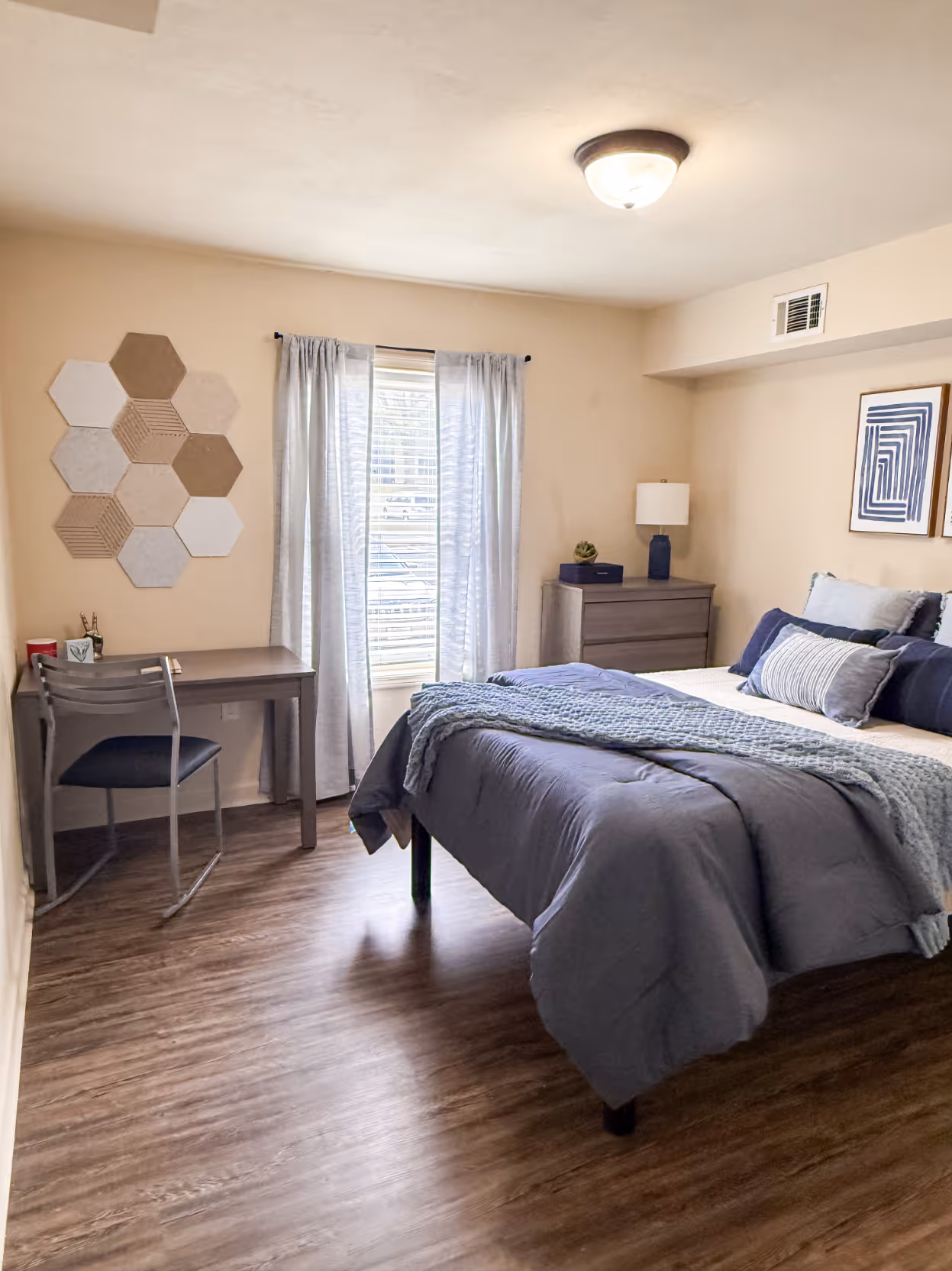 Student apartment bedroom with a bed, desk, featuring a vibrant modern wall art at Rev Oxford in Oxford, MS.