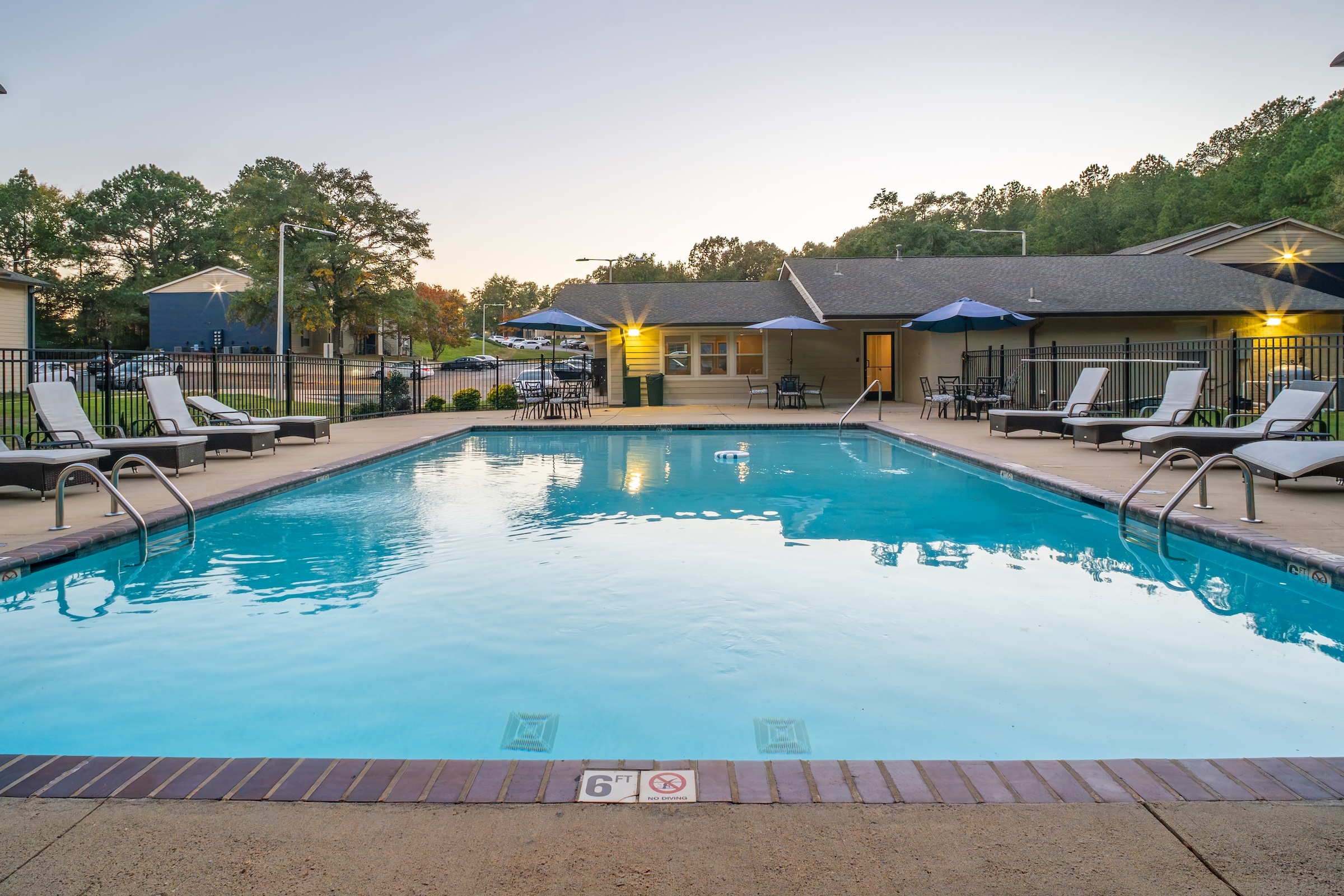 Large community swimming pool with lounge chairs, tables, and umbrellas, showcasing the outdoor amenity area at Rev Oxford in Oxford, MS.