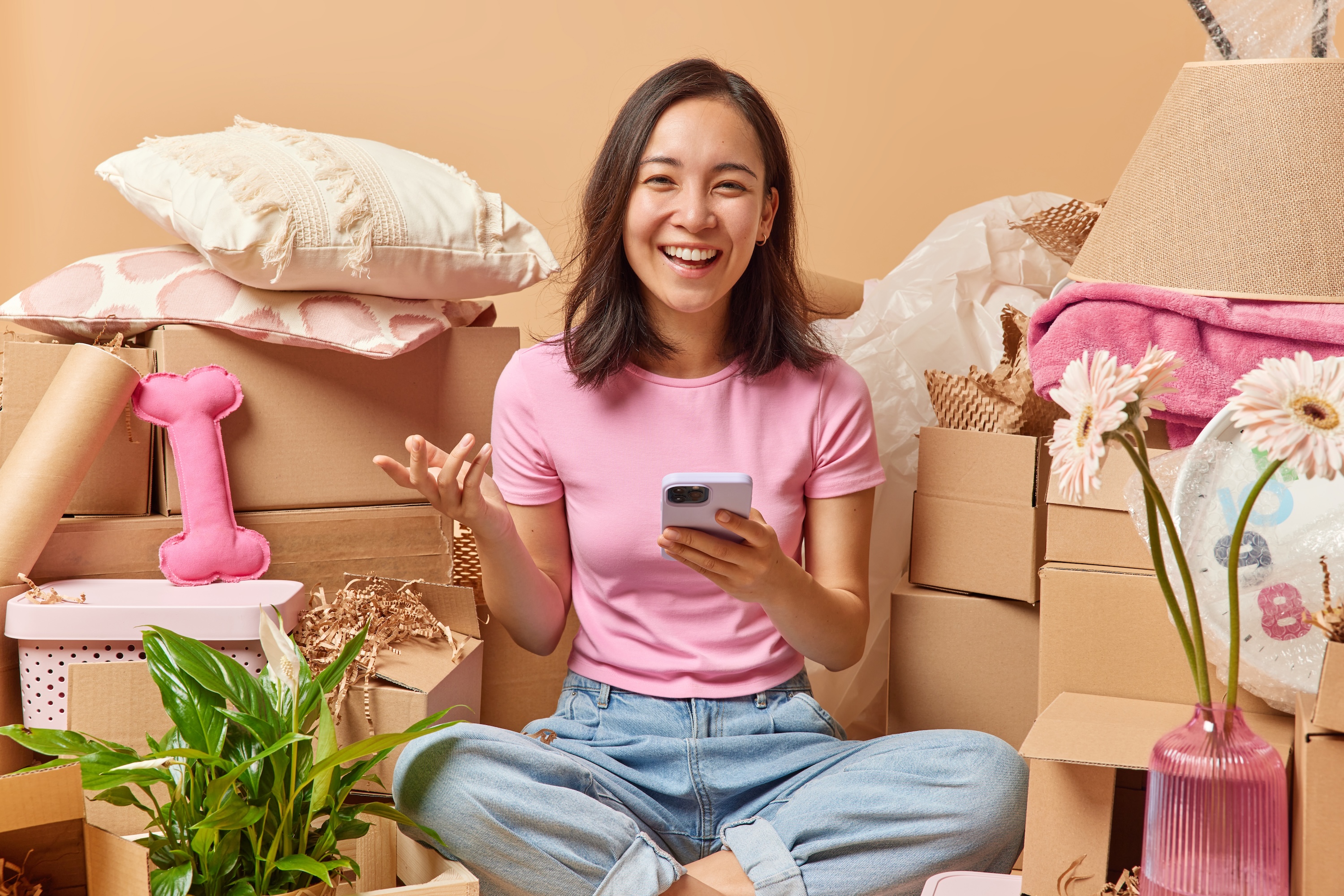 A happy resident holding a smartphone while surrounded by moving boxes symbolizing the moving process of students in Oxford, MS.