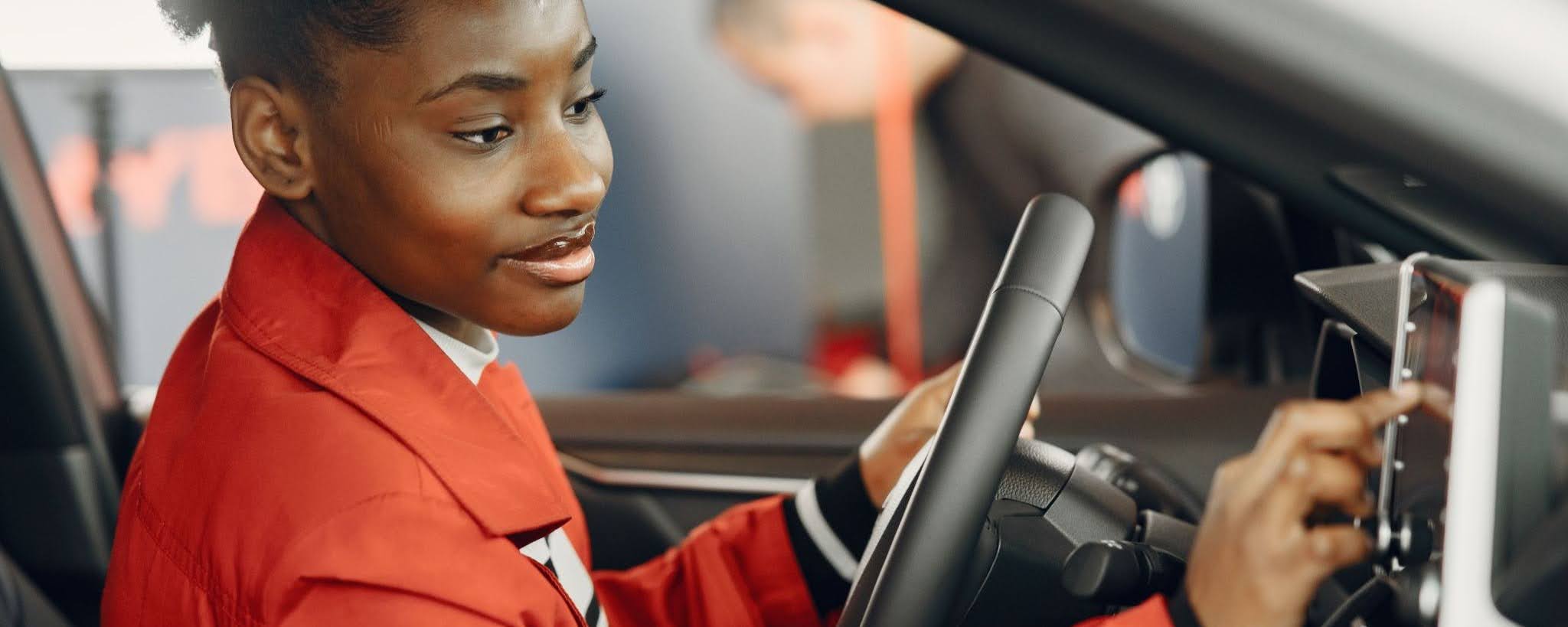 Person in a red jacket adjusting the touchscreen while seated behind the steering wheel of a car