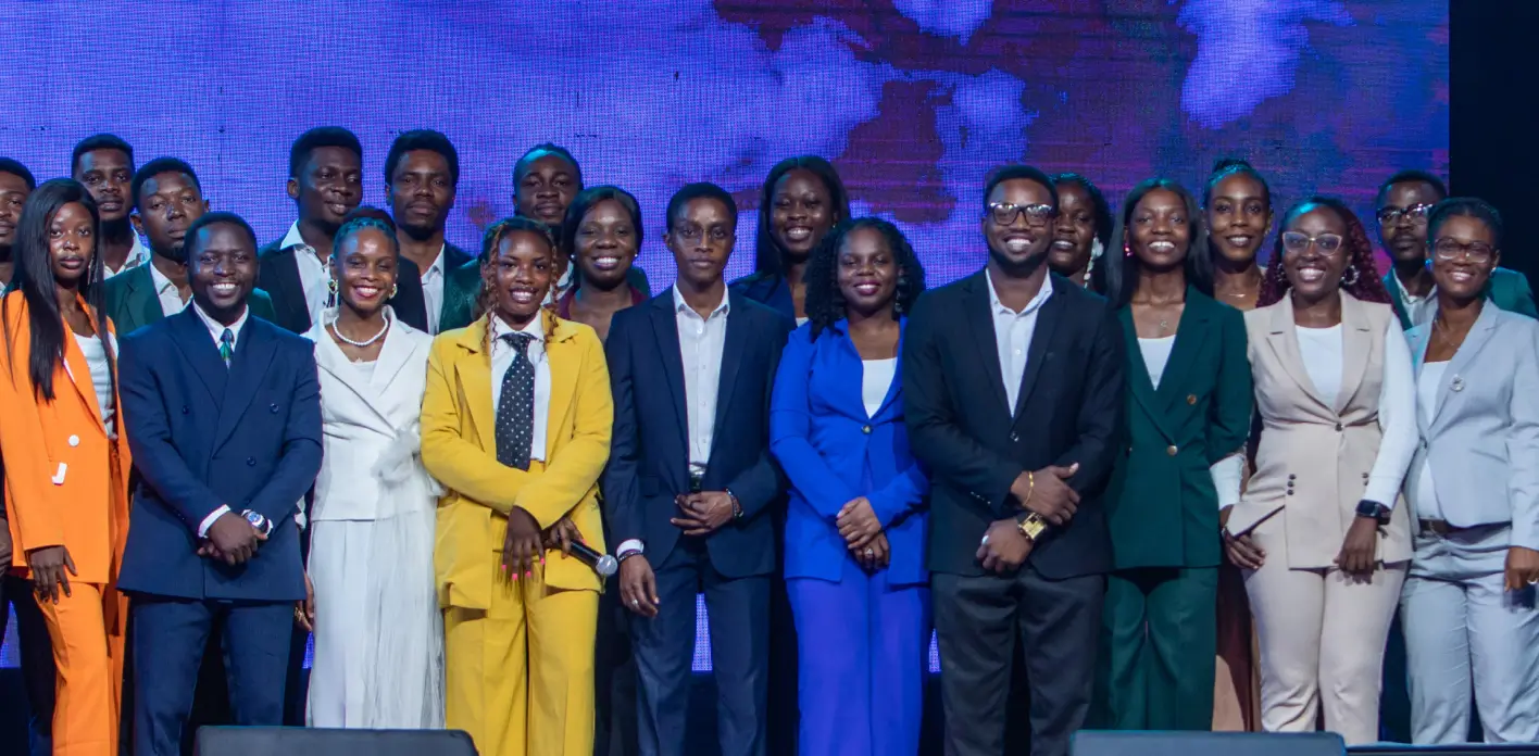 Group of professionally dressed men and women posing on stage in front of a blue and purple digital backdrop.