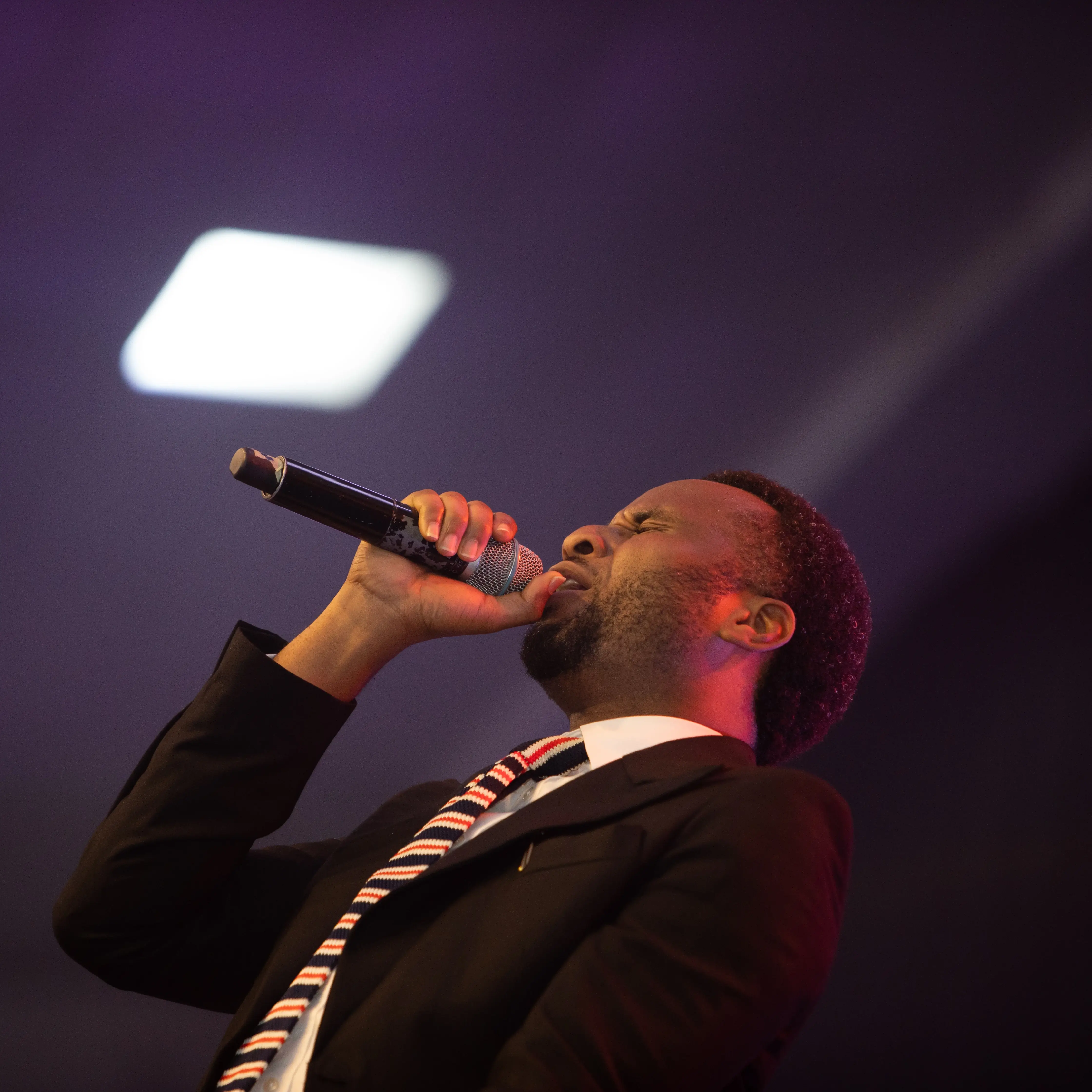 Man in a suit and striped tie passionately singing into a microphone on stage.