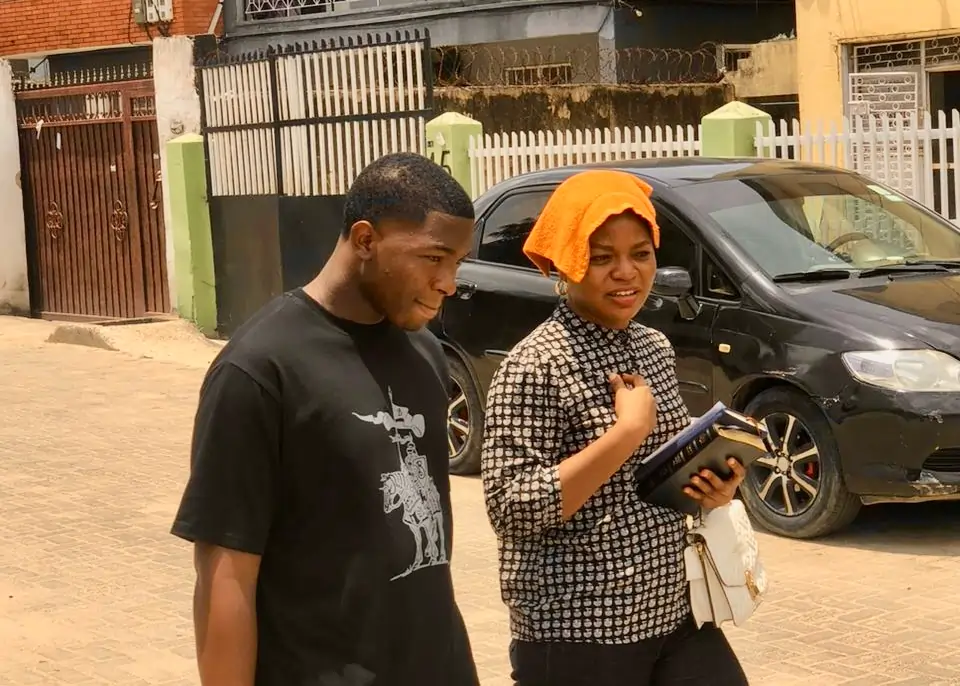 A man in a black t-shirt and a woman with an orange headscarf hold a book while walking outdoors.