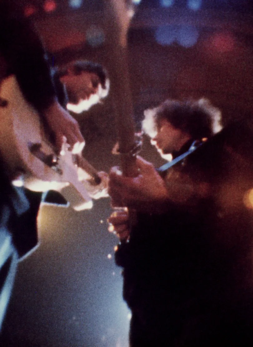 Two guitarists facing each other as they play on a live stage.