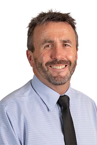 A man in a blue shirt and tie smiling. 
