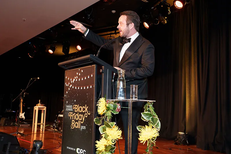 Auctioneer on stage speaking to crowd at Black Friday Ball. 