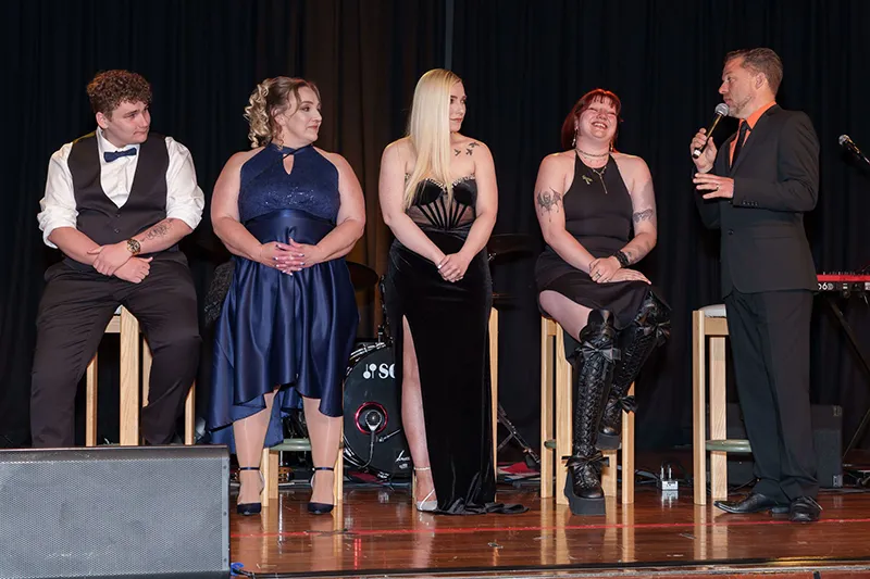 Line of people sitting on chairs on stage preparing to speak at Black Friday Ball. 