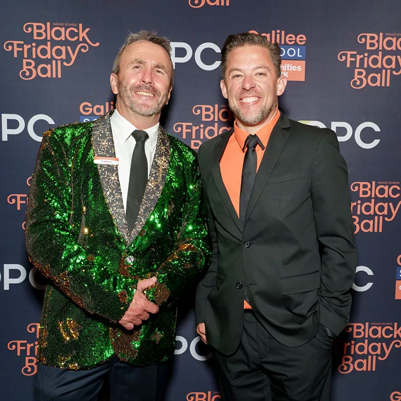 Two people shaking hands in front of Black Friday Ball photo wall