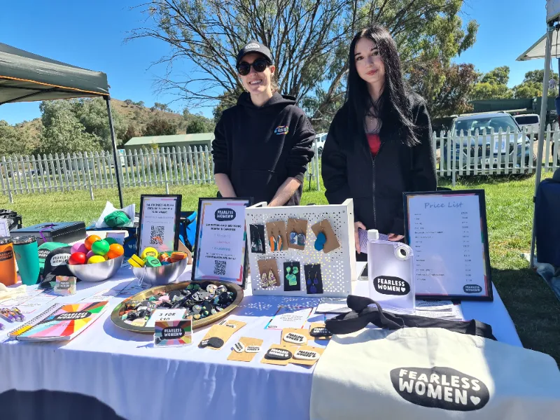 Two people posing behind the Fearless Women market stall table