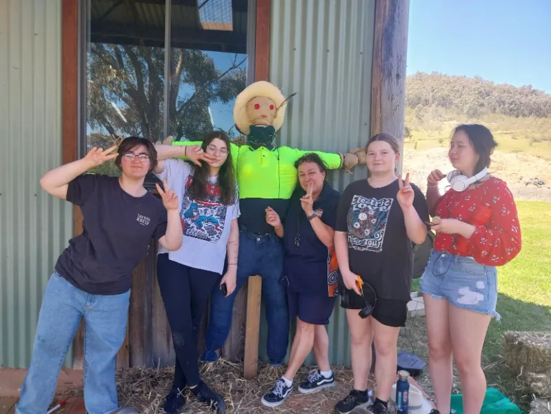 A group of people posing with a scarecrow.