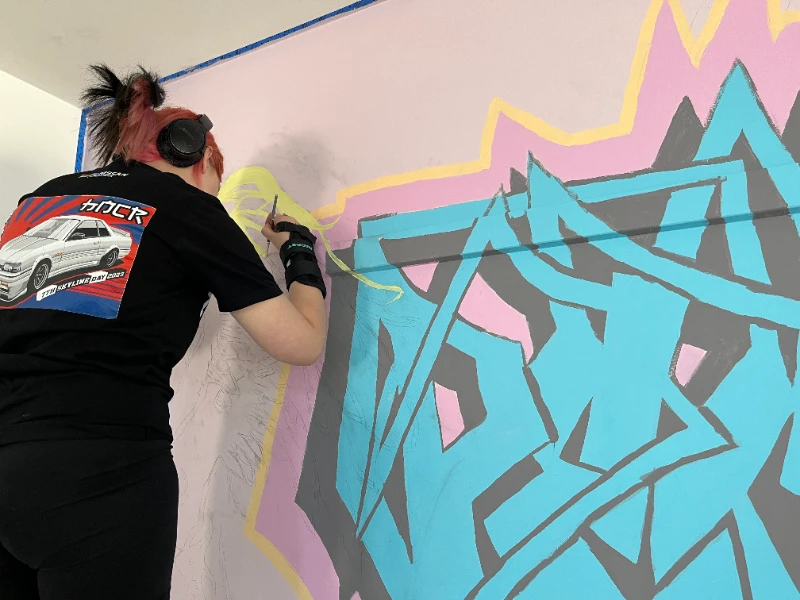 Person in the progress of painting mural artwork on wall. 