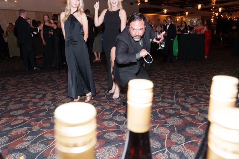 A man in a suit about to toss a ring over a bottle of wine at the Black Friday Ball. 