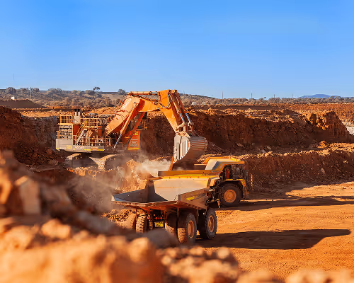 Large orange excavator loading dirt into an articulated dump truck at an open mining site under a clear blue sky.