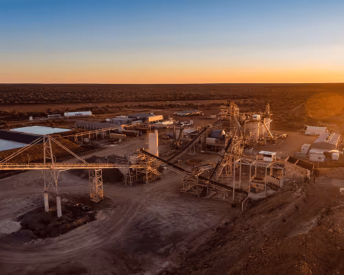 Industrial mining site with conveyor belts and processing equipment at sunset in a desert landscape.